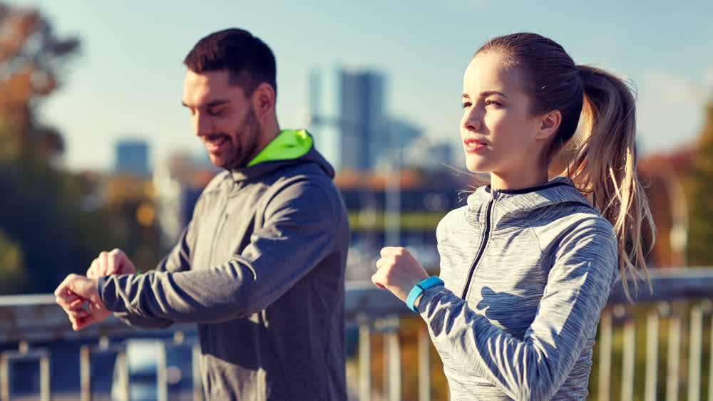 Mann und Frau joggen und tragen Fitnesstracker.