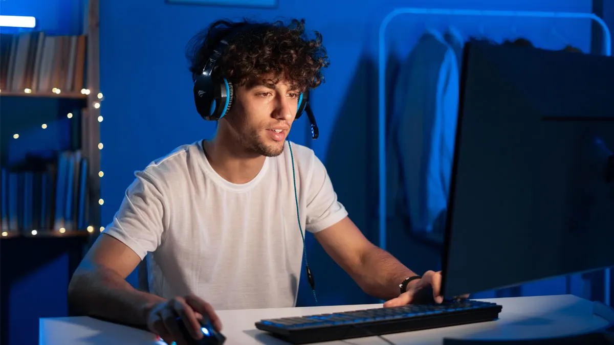 Eine Person mit Kopfhörern spielt an einem Computer mit Tastatur und Maus auf einem Schreibtisch.