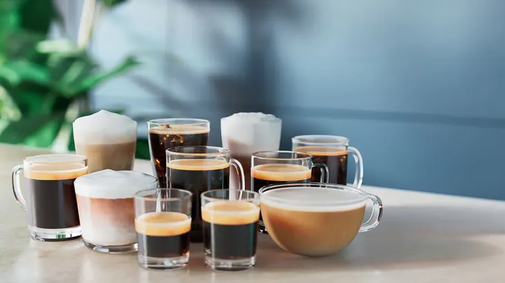 Eine Sammlung von Kaffeegetränken in Glasbehältern, darunter Espresso, Cappuccino und Eiskaffee, auf einem Tisch.