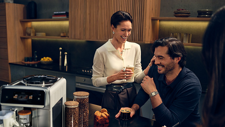 Ein Mann und eine Frau sind lächelnd in einer Küche und trinken Kaffee.