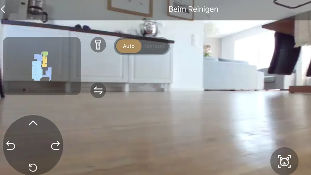 Ansicht durch die Kamera eines Roboterstaubsaugers auf einen Holzboden in einem Raum mit Möbeln und Bedienelementen.