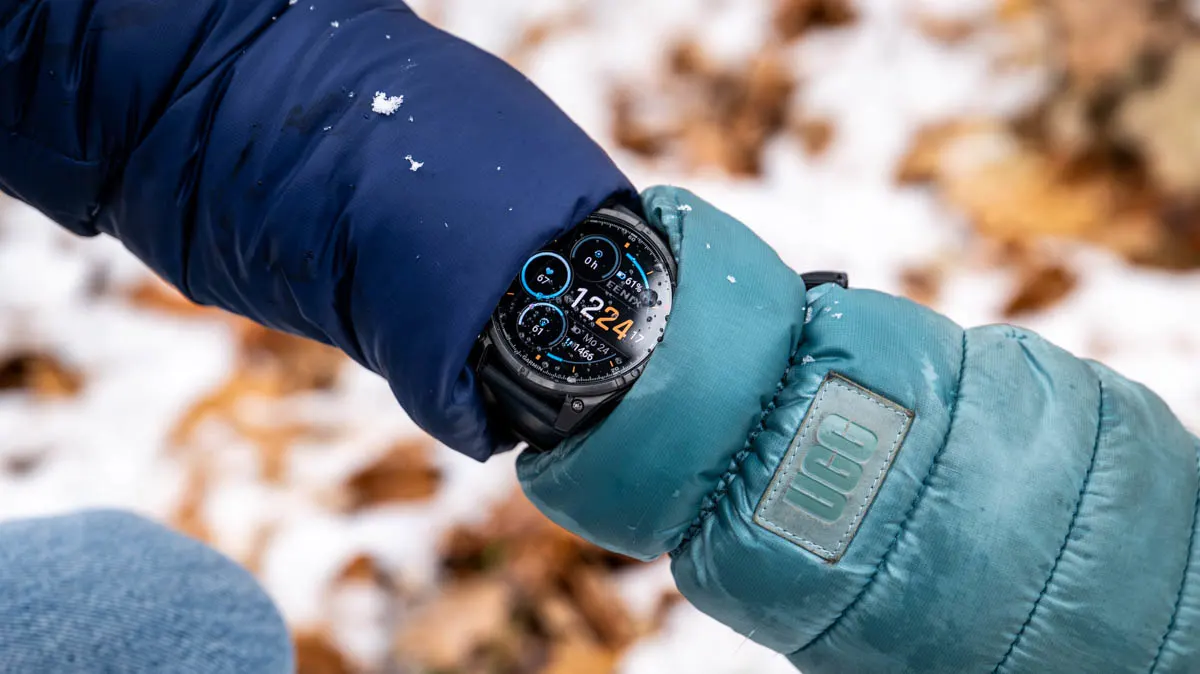 Die Garmin Fenix 8 Pro guckt an Franzis Arm zwischen Winterjacke und Handschuh hervor, auf dem Display ein paar Tropfen geschmolzener Schnee.