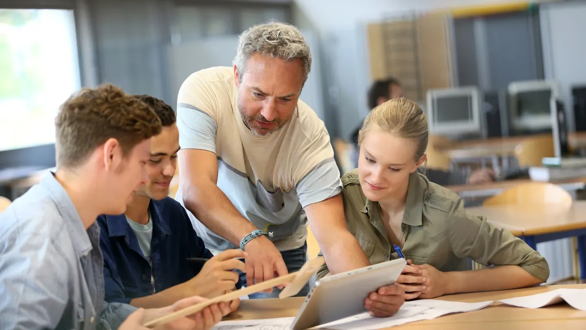 Ein Lehrer und drei Schüler blicken gemeinsam auf ein Tablet.
