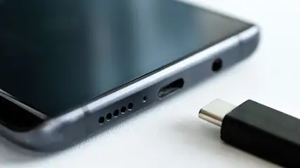 Nahaufnahme eines Smartphones mit USB-C-Anschluss und Lautsprecheröffnungen neben einem schwarzen USB-C-Kabel auf weißem Hintergrund.
