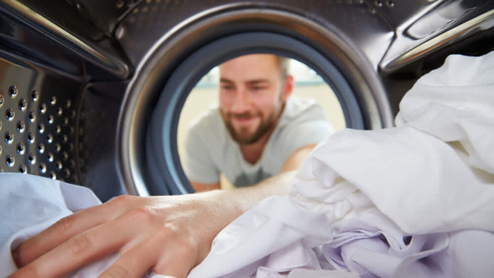 Ein Mann greift in eine Waschmaschine mit weißen Hemden.