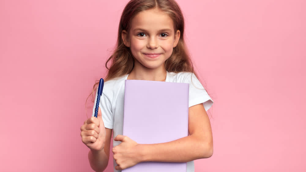 Mädchen mit Tagebuch und Stift vor pinkem Hintergrund
