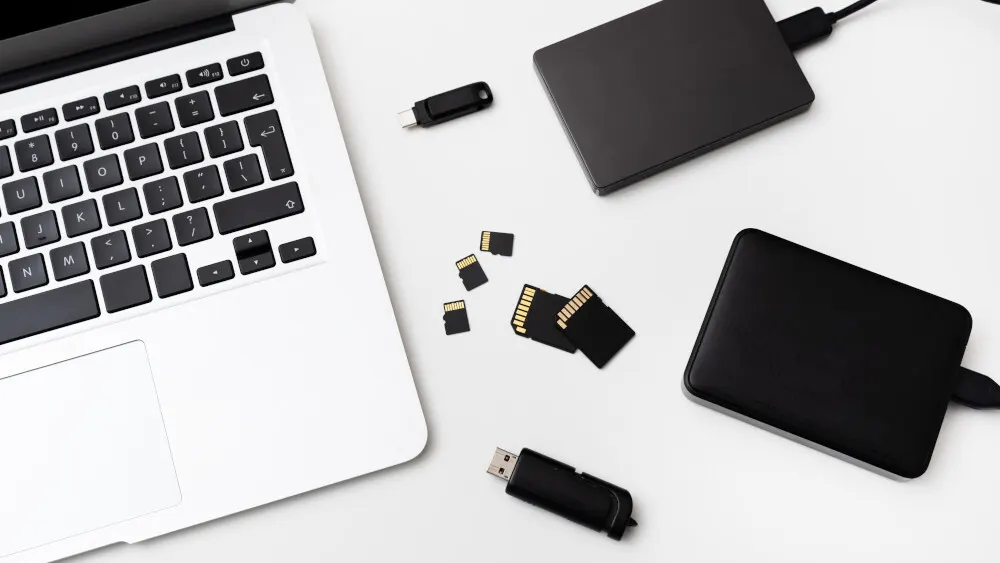 Auf einer weißen Fläche liegen ein Laptop, zwei schwarze Festplatten, zwei USB-Sticks und vier SD-Karten.