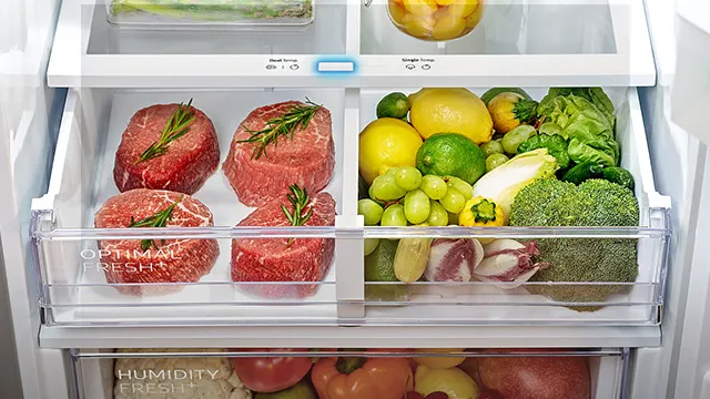 Ein offener Kühlschrank zeigt Fleischstücke mit Rosmarin, Zitronen, Limetten, Trauben und Brokkoli in durchsichtigen Schubladen.