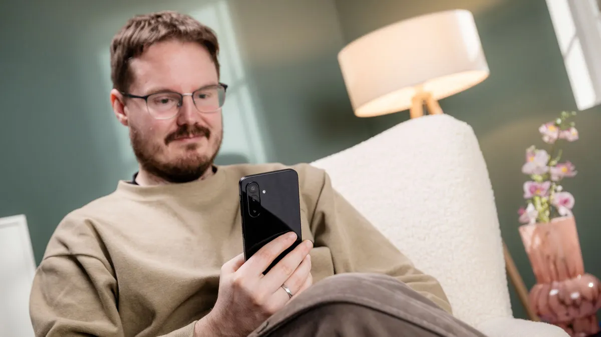Michael sitzt entspannt in einem Wohnzimmer und blickt auf das Display des Samsung-Smartphones Galaxy A26 5G.
