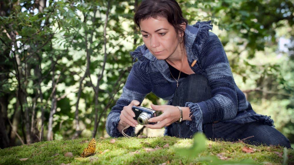 Eine Frau fotografiert einen Schmetterling mit einer Kompaktkamera.