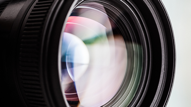 Nahaufnahme eines schwarzen Kameraobjektivs mit farbigen Reflexionen auf dem Glas.
