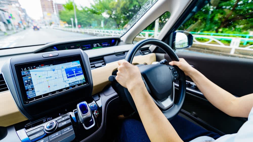 Eine Person lenkt ein Auto mit Navigationssystem im Dashboard.