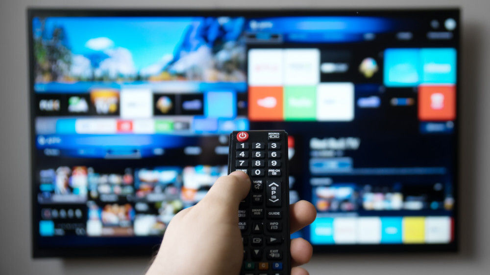 Eine Person hält die Fernbedienung in der Hand und richtet sie auf den Fernseher.