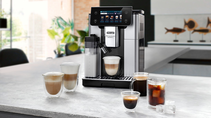 Auf einer Küchentheke steht eine Kaffeemaschine neben zwei Tassen Kaffee. Eine Schale Müsli und rote Johannisbeeren stehen davor.