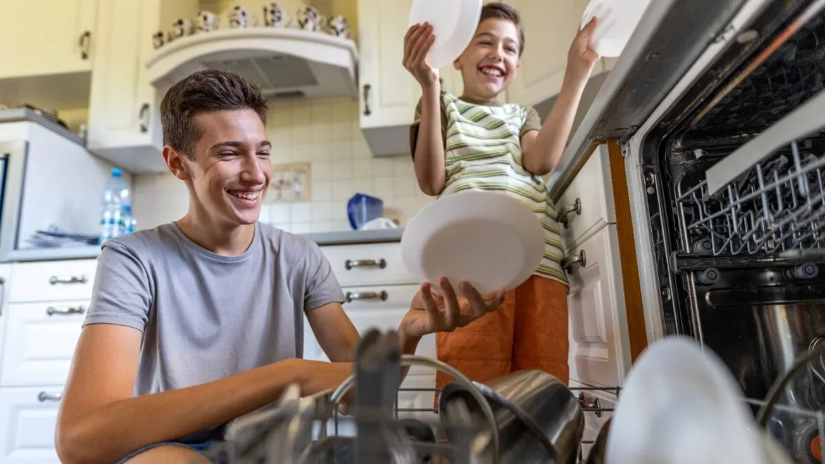 Zwei Jungen nehmen Geschirr aus einem Geschirrspüler.