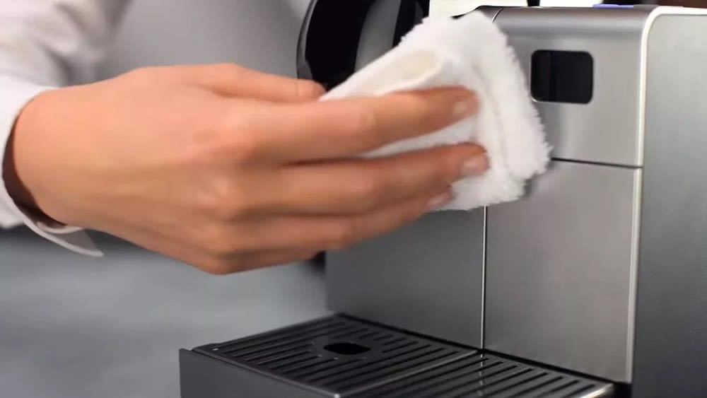 Eine Person reinigt mit einem weißen Tuch eine Kaffeemaschine.
