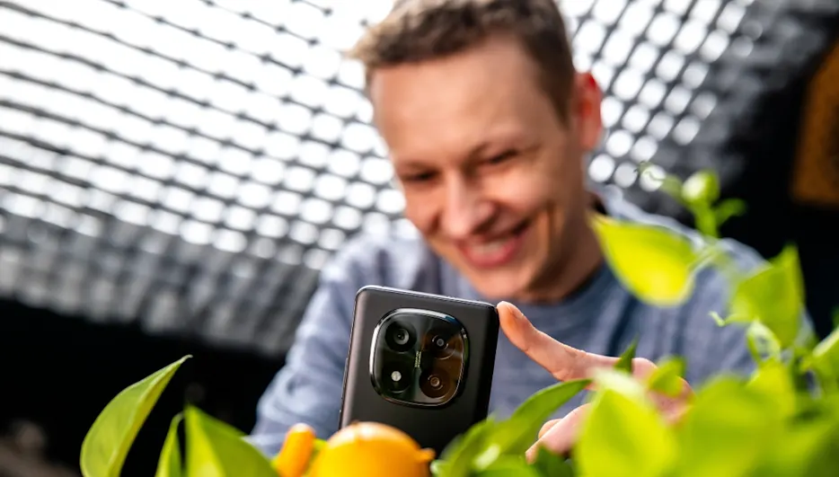 Ein Mann blickt auf ein schwarzes Smartphone mit drei Objektiven, umgeben von grünen Blättern und gelben Zitronen.