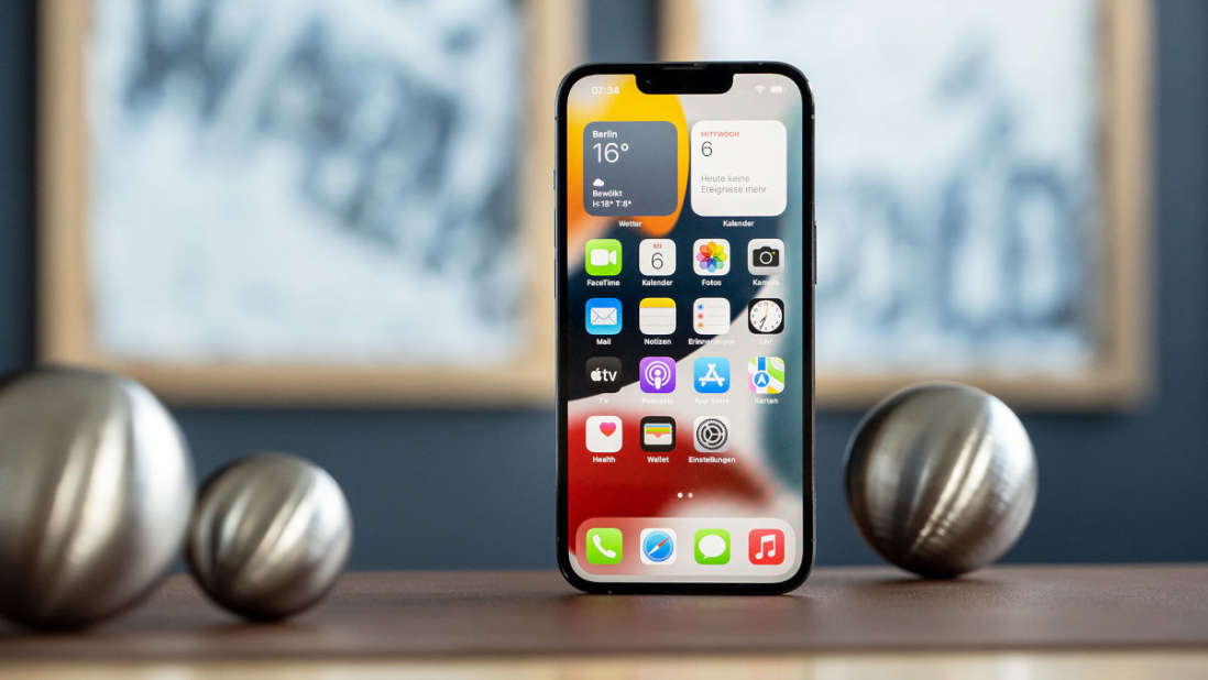 Das iPhone 13 liegt mit angeschaltetem Display auf einem Tisch mit drei Stahlkugeln.