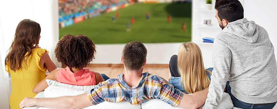 Eine Gruppe Erwachsener sitzt auf dem Sofa vorm Fernseher und schaut Fußball.
