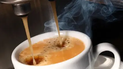 Espresso fließt aus einer Maschine in eine weiße Tasse, Dampf steigt auf, mit dunklem Hintergrund.