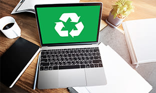 Ein Laptop mit grünem Bildschirm und weißem Recycling-Symbol steht auf einem Holzschreibtisch.