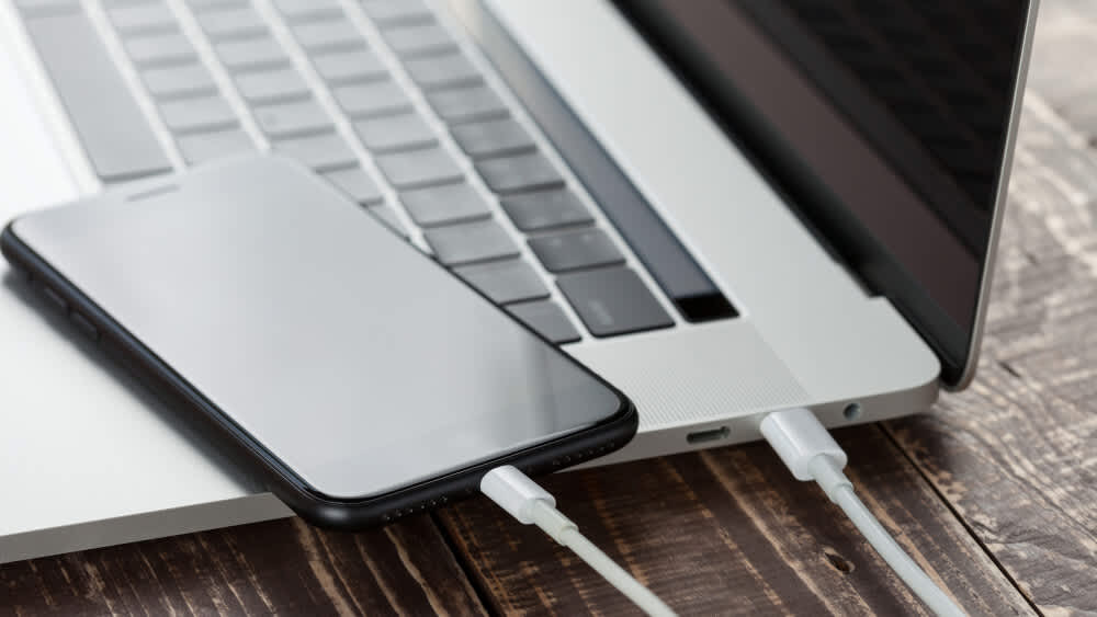 Ein iPhone und ein MacBook sind über ein Kabel miteinander verbunden. 