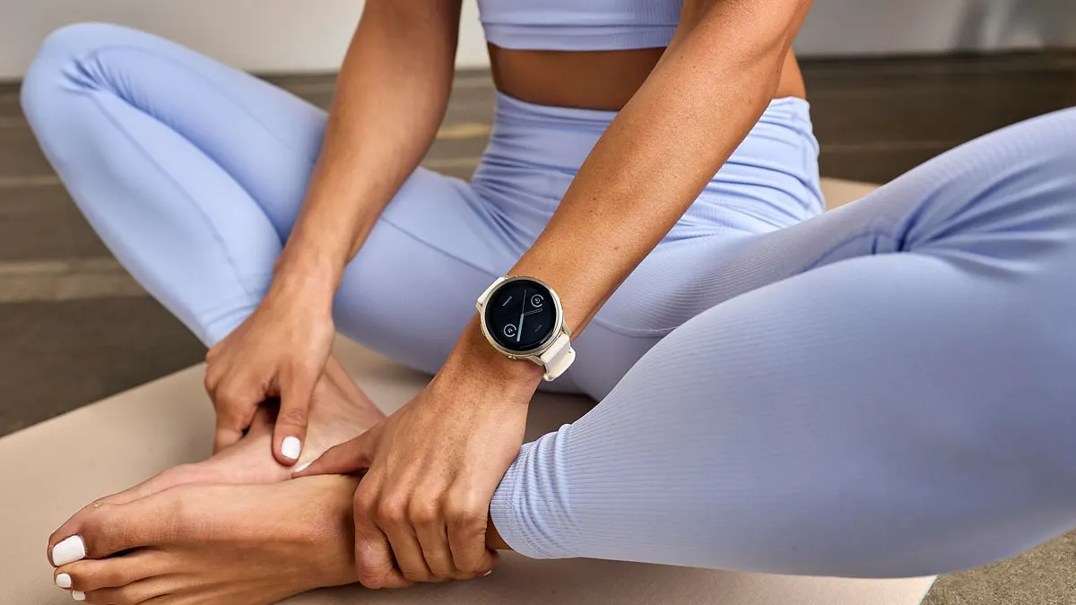 Eine Frau in Sportkleidung trägt eine Smartwatch und sitzt im Schmetterlingssitz auf einer Yogamatte.