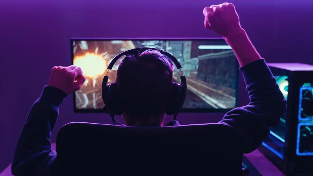 Ein Mann streckt die Arme in die Höhe vor einem Schreibtisch mit Monitor und Gaming-PC.