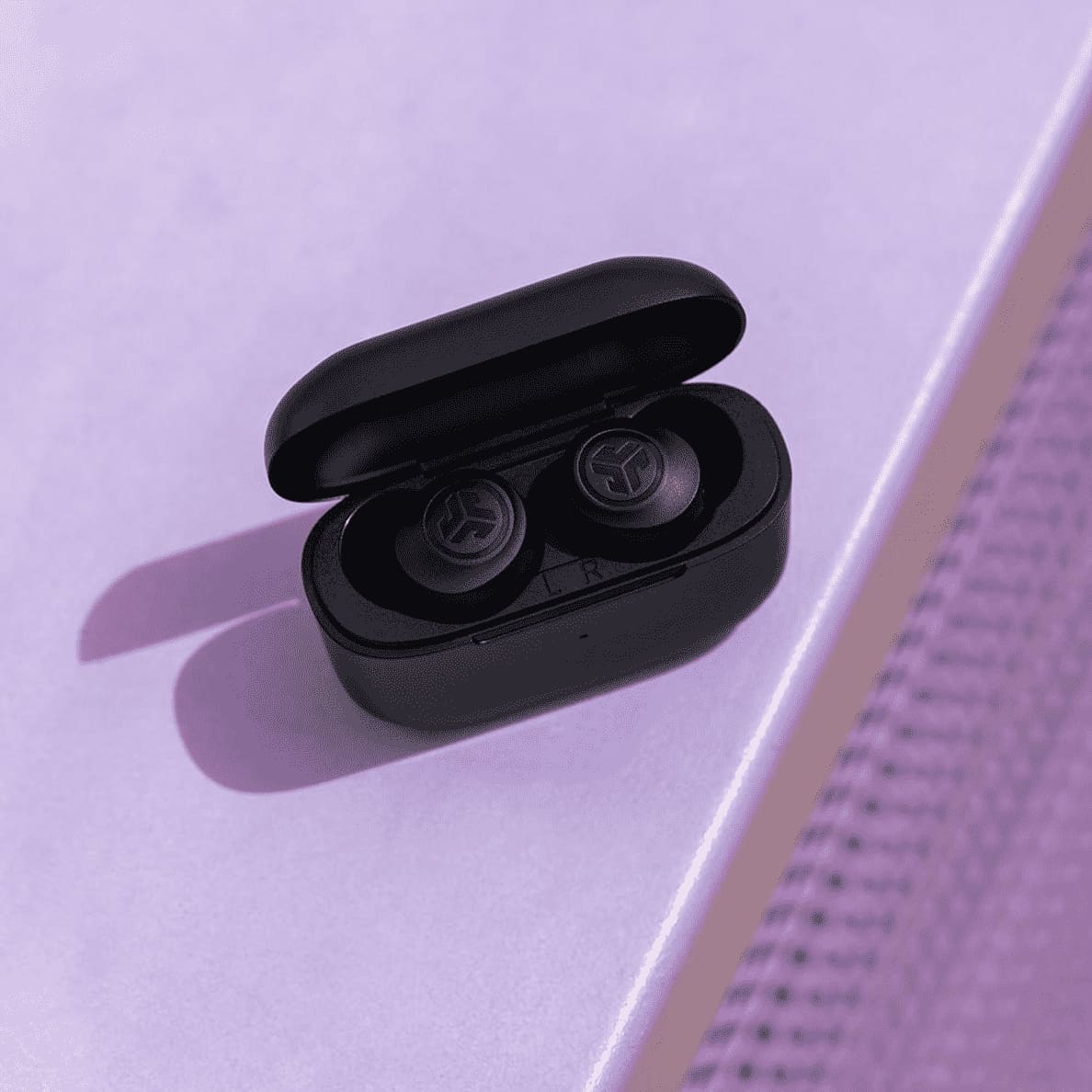 JLAB Go Air Pop True Wireless, In-ear Kopfhörer schwarz sind im offenem Ladecase liegen auf einer lila Oberfläche