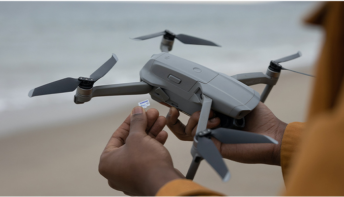 Nahaufnahme einer Drohne. Im Vordergrund hält eine Hand eine Samsung Speicherkarte ins Bild.