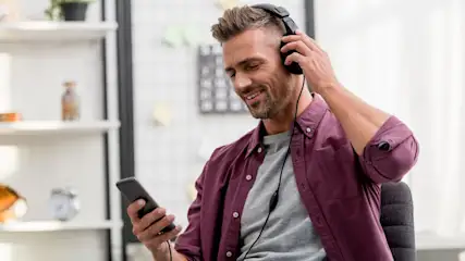 Ein Mann sitzt auf einem Stuhl und hört Musik über Kopfhörer.