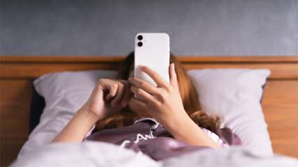 Frau nutzt iPhone im Bett liegend