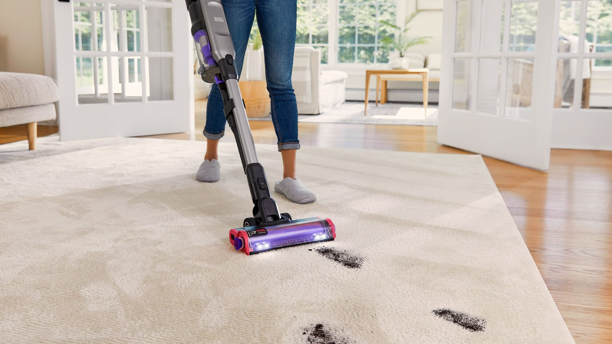 Eine Person saugt einen beigen Teppich mit einem Staubsauger. Auf dem Teppich sind dunkle Flecken zu sehen.