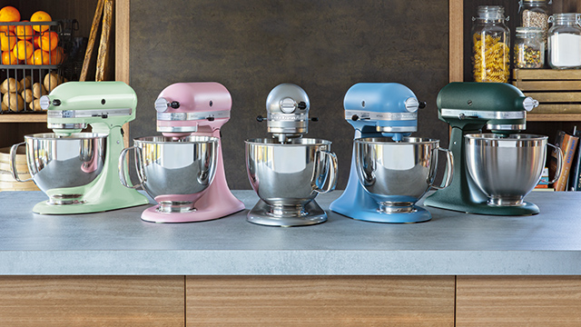 Fünf Küchenmaschinen in Grün, Rosa, Silber, Blau und Dunkelgrün mit Edelstahlschüsseln stehen auf einer Küchentheke.