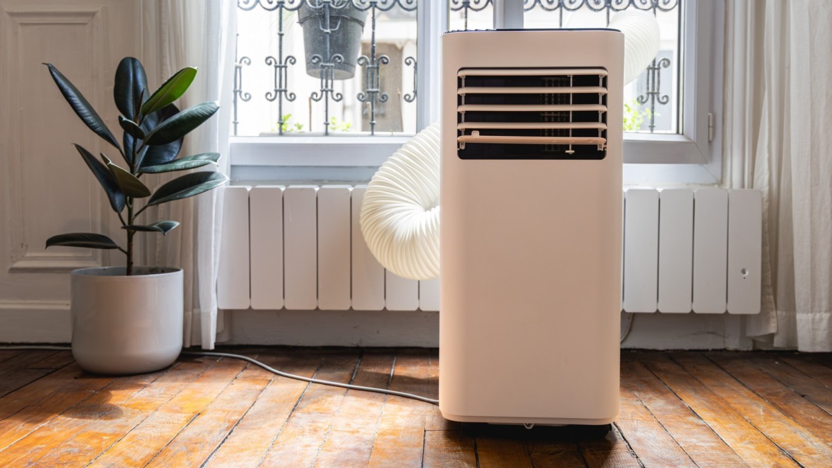 Eine mobile Monoblock-Klimaanlage steht in einem Innenraum. Durch ein Fenster führt der Abluftschlauch.