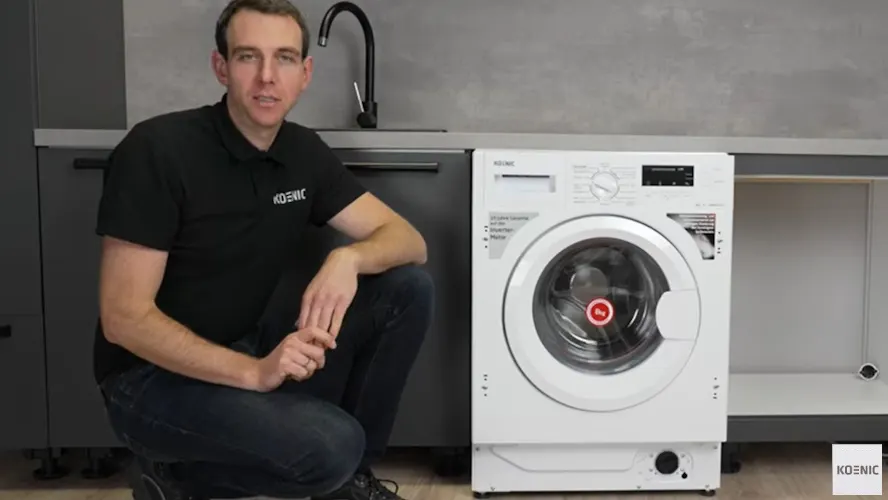 Ein Experte der Marke KOENIC sitzt neben einer Waschmaschine, die er gerade einbaut.