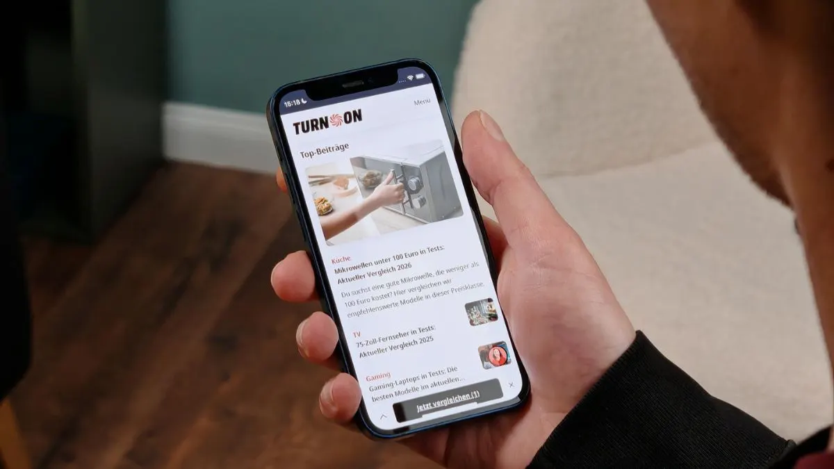 Alex hält ein iPhone 12 mini mit 5,4-Zoll-Display in der Hand und legt den Daumen seitlich an das Handy.