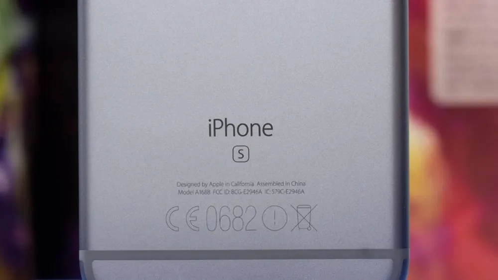 Nahaufnahme der Rückseite eines grauen iPhone S mit Herstellerinformationen und Zertifizierungszeichen.