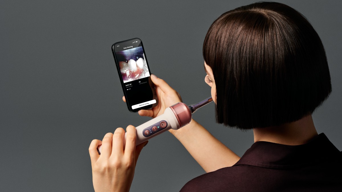 Eine Frau nutzt die Zahnbürste Dyson CameraJet, während sie die Live-Funktion auf dem Smartphone nutzt.