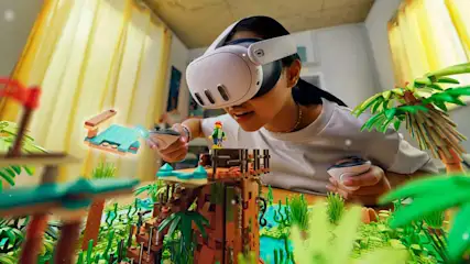 Eine Person mit VR-Headset und Controllern interagiert mit einem Lego-Diorama einer tropischen Szene auf einem Tisch.