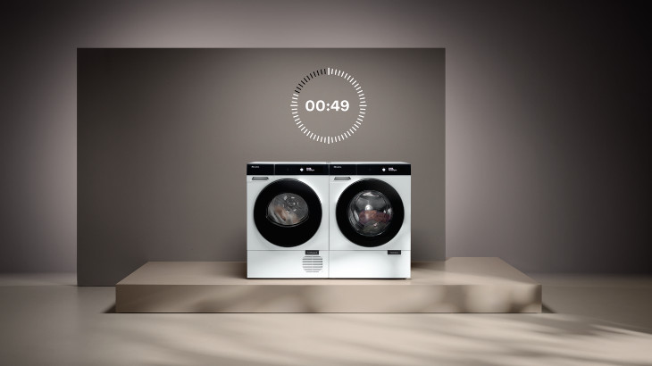Zwei weiße Waschmaschinen stehen auf einer Plattform vor einer grauen Wand mit einem digitalen Timer darüber.