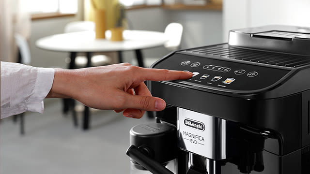 Eine Person drückt auf den Touchscreen einer Delonghi Kaffeemaschine.