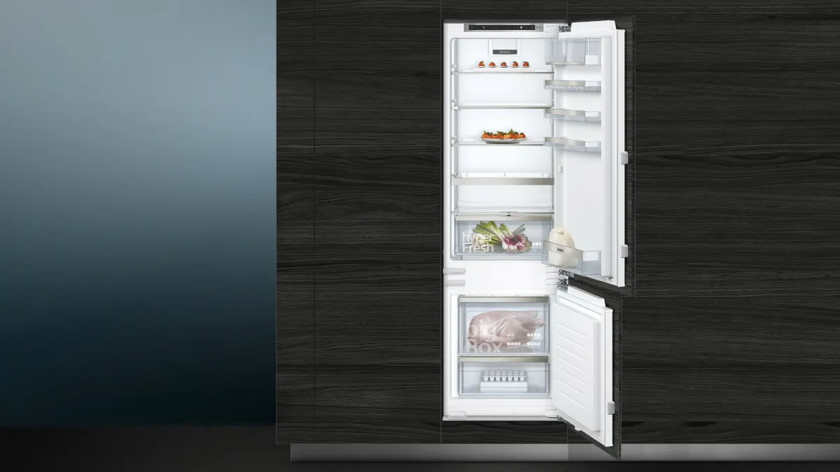 Die Einbau-Kühl-Gefrierkombination Siemens KI87SADD0 iQ500 mit geöffneten Türen in einer dunklen Küchenzeile.