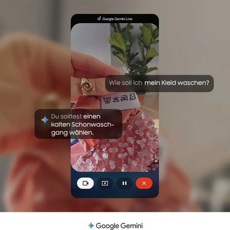 Eine Demonstration der "Google Gemini Live"-Funktion auf einem Smartphone. Eine Person hält das Pflegeetikett eines rosa Paillettenkleides in die Kamera und stellt die Frage: "Wie soll ich mein Kleid waschen?". Google Gemini analysiert die sichtbaren Waschsymbole und gibt die Antwort: "Du solltest einen kalten Schonwaschgang wählen." Am unteren Bildrand ist das Logo von Google Gemini zu sehen.
