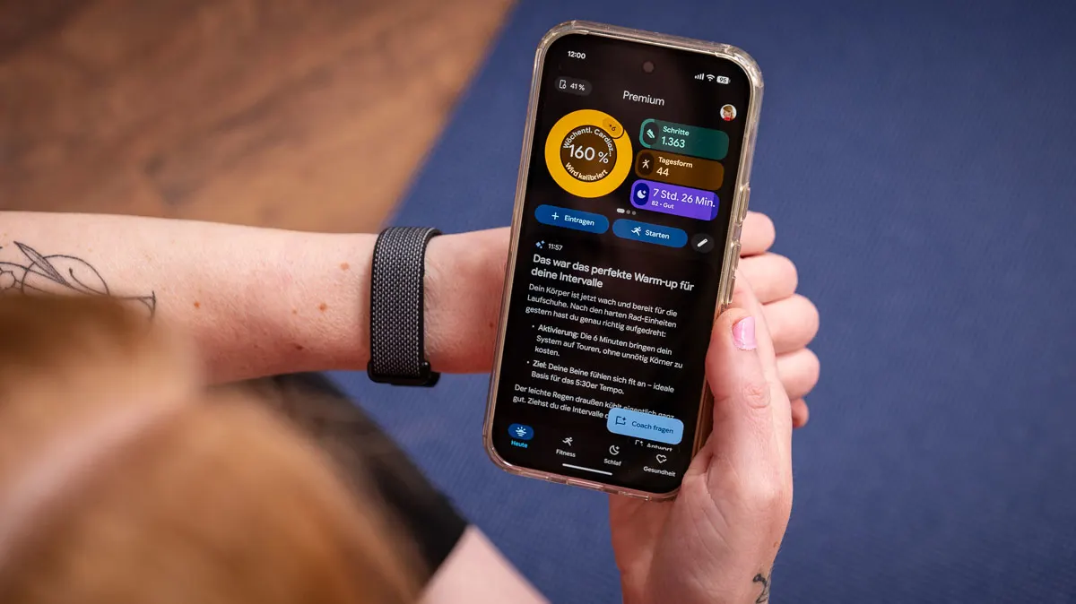 Franzi schaut sich die Startseite der Google-Health-App auf dem Smartphone an, am linken Handgelenk trägt sie das Fitbit Air.