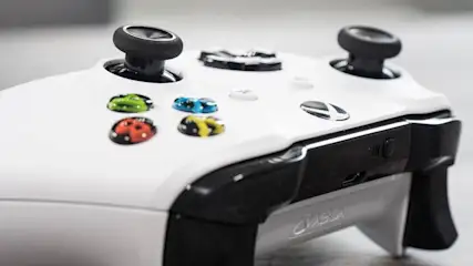 Nahaufnahme eines weißen Xbox-Controllers mit schwarzen Joysticks und farbigen Tasten.