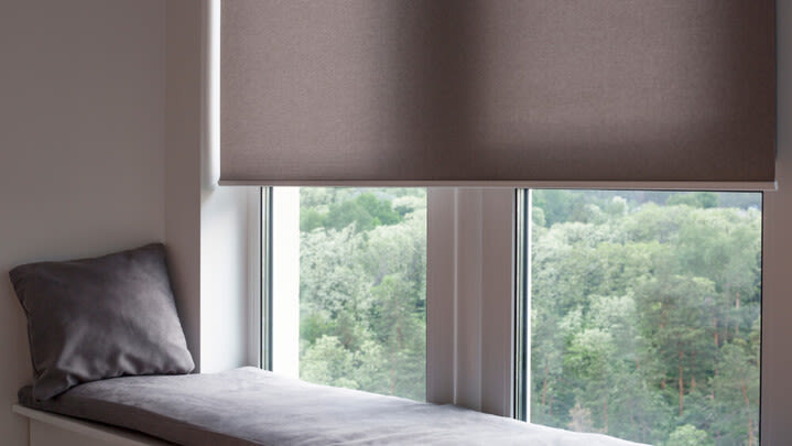 Ein Fenster hinter einer Sitzecke mit Sitzkissen wird zur Hälfte von einem Rollo verdeckt.