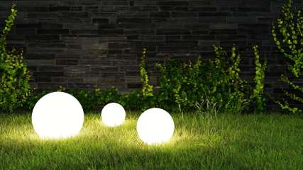 Drei Lampen leuchten auf dem Rasen im Garten bei Nacht.