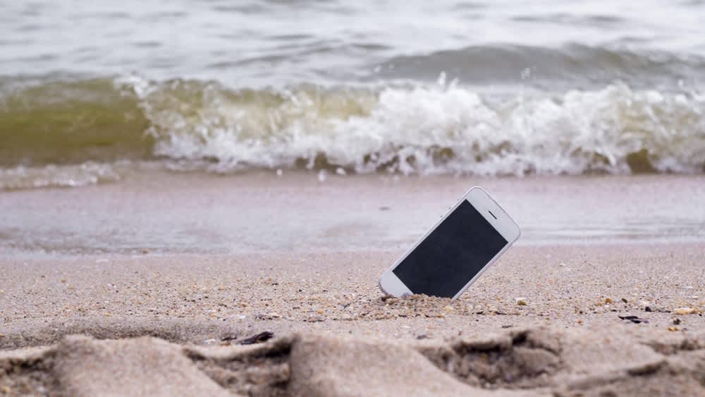 Ein iPhone steckt am Strand im Sand.