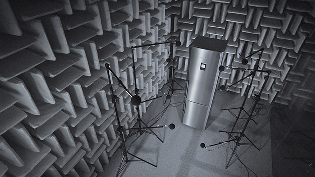 Ein schalltoter Raum mit Noppen an den Wänden, Mikrofonen auf Stativen und einem zylindrischen Objekt in der Mitte.